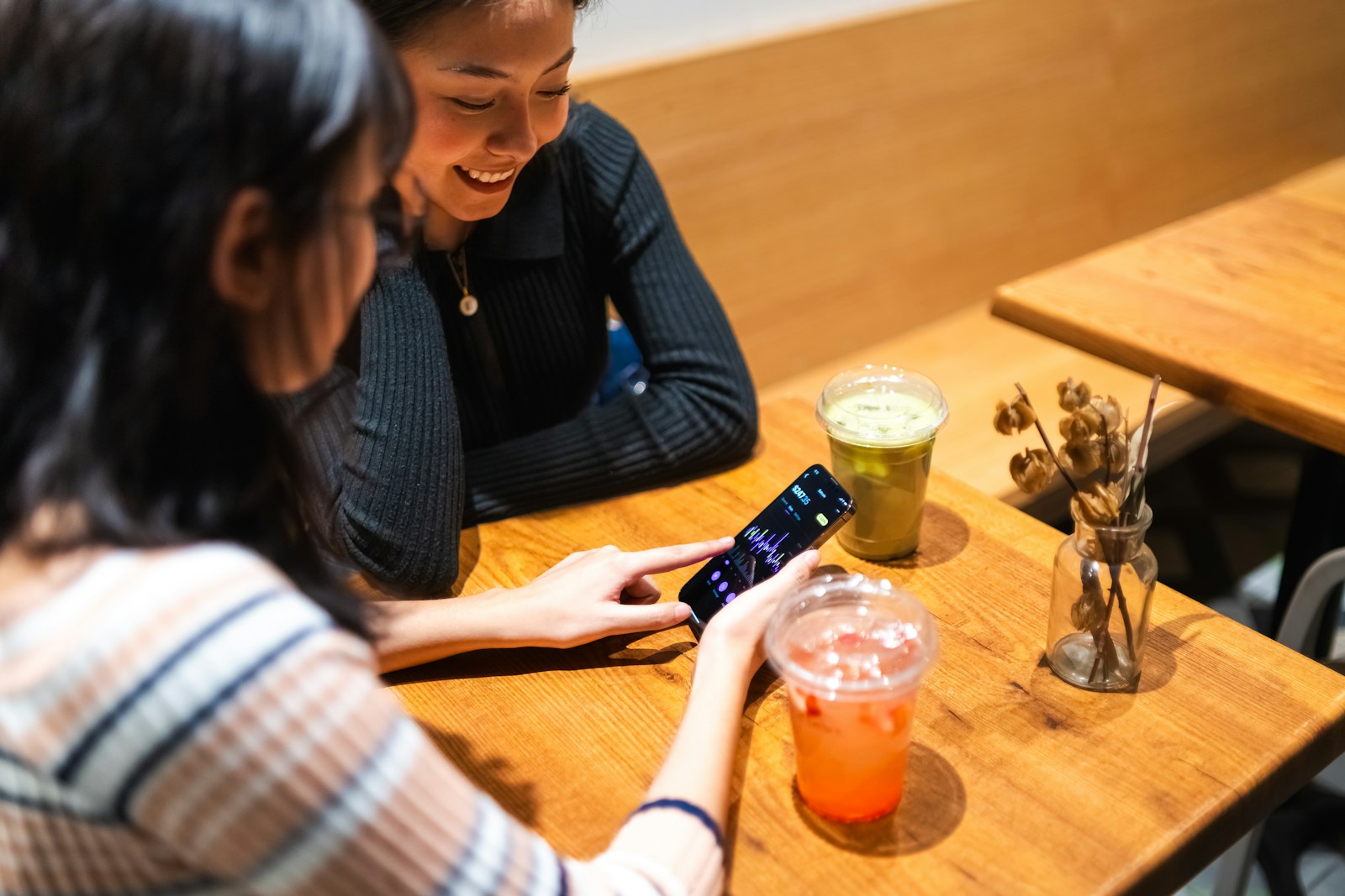 Duas clientes sorrindo olhando o celular numa cafeteria, o tipo de momento em que uma avaliação no Google acontece.