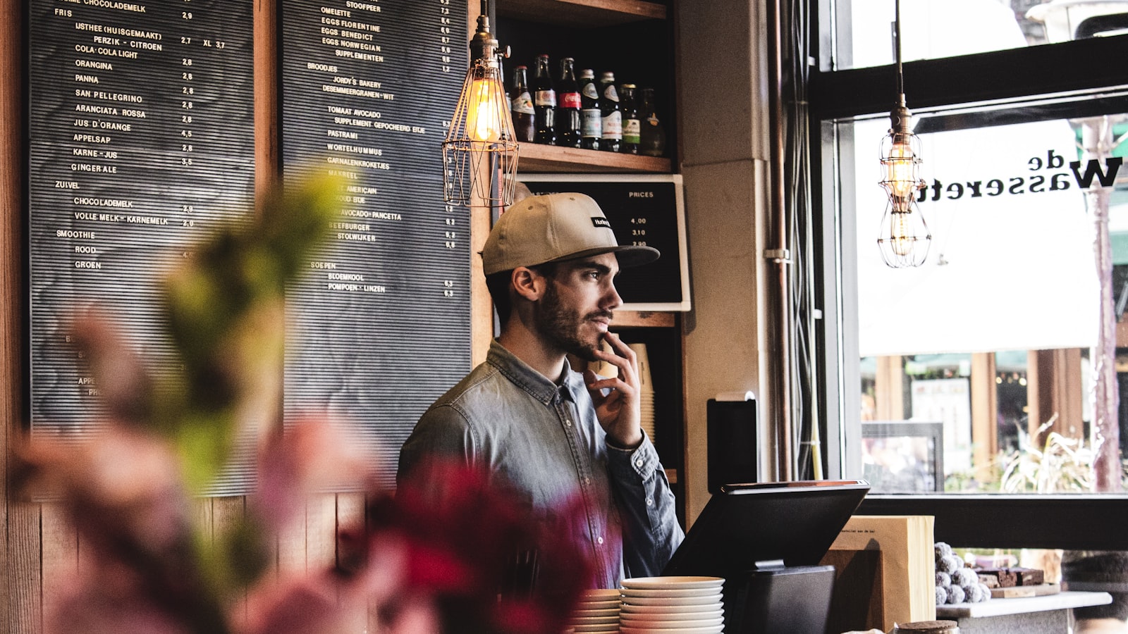 A cafe owner at the counter by a chalkboard menu, ready to ask customers for feedback