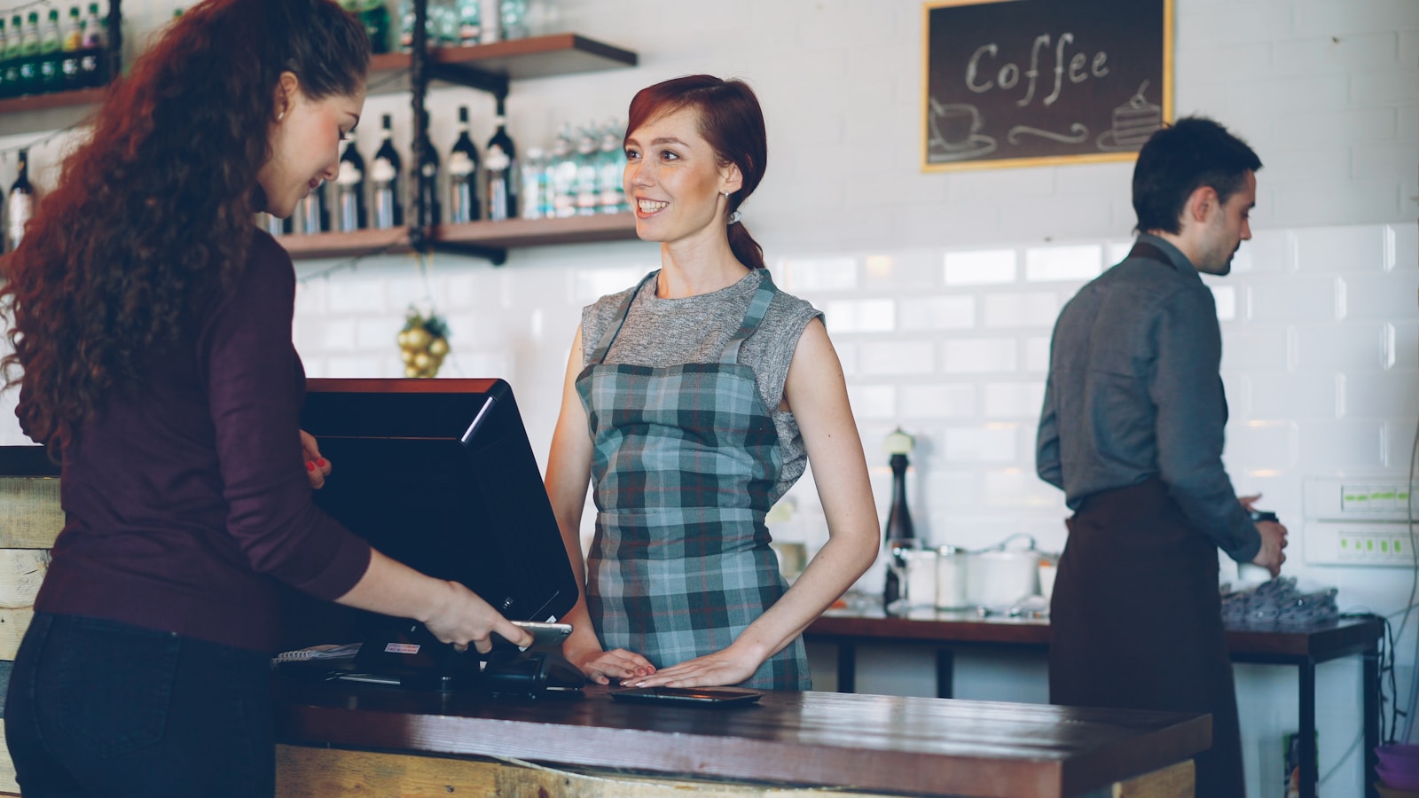 Customer paying at a cafe counter with a smartphone, replacing a paper loyalty card with a digital one